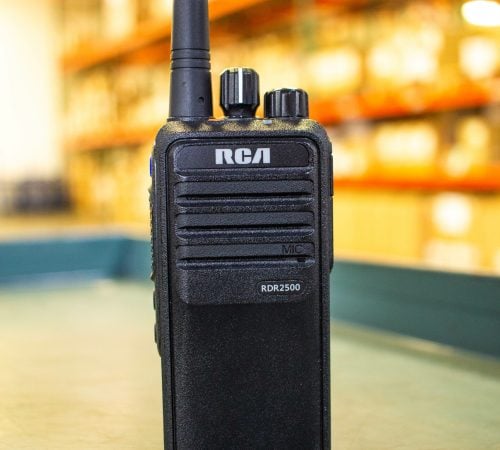 An RCA RDR2500 handheld two-way radio sits upright on a table inside a warehouse.